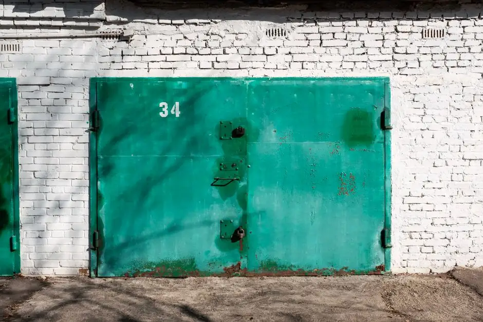 Close-up of a weathered green metal door on a white brick wall with number 34.
